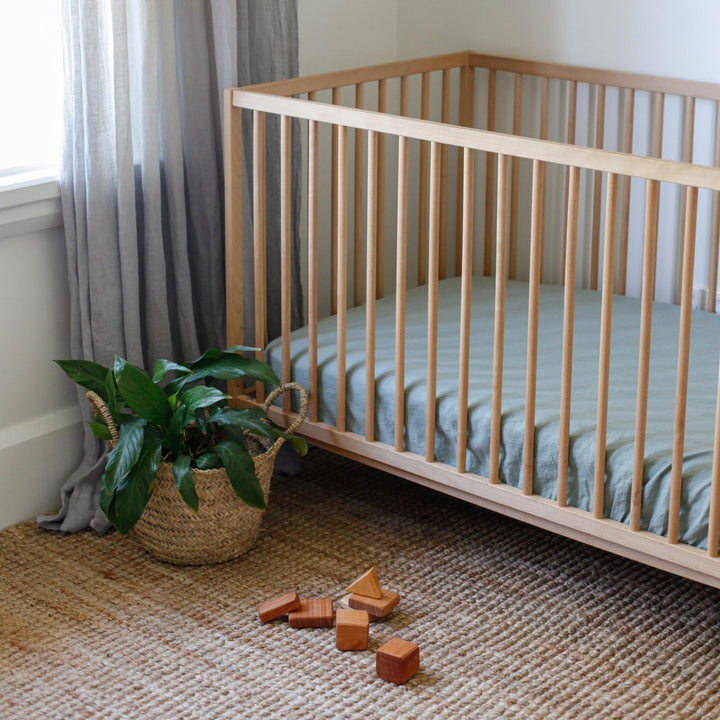 Foxtrot Home French Flax Linen styled in a baby's bedroom with Sage Green Cot Sheet and Bassinet Sheets.