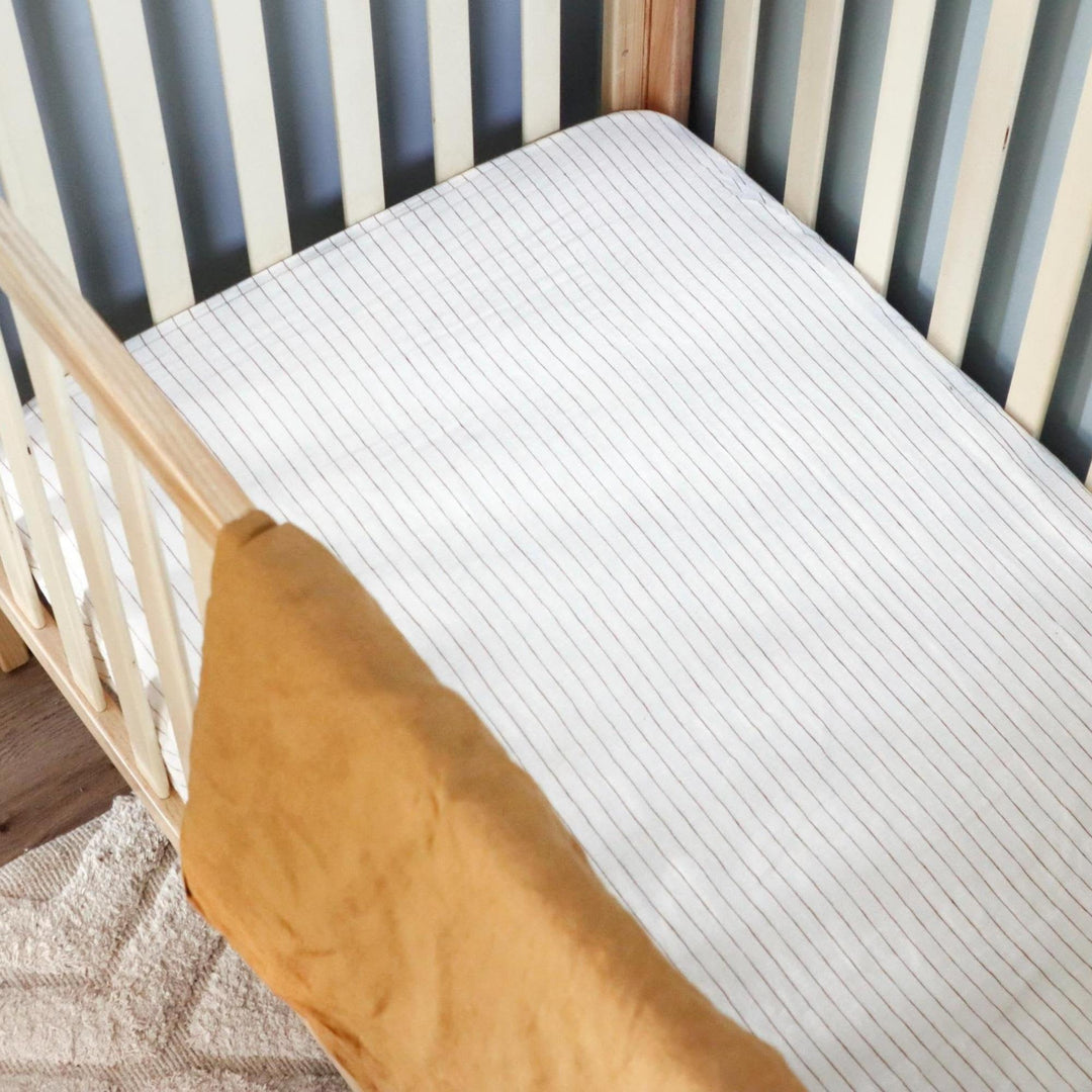 Foxtrot Home French Flax Linen styled in a baby's bedroom with Tobacco Stripes Cot Sheet and Bassinet Sheets.